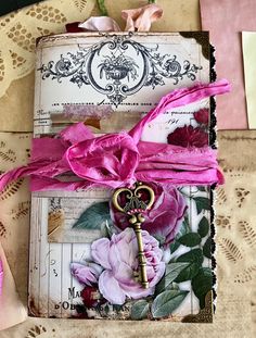 an open book with a key and pink ribbon on it sitting on a lace doily