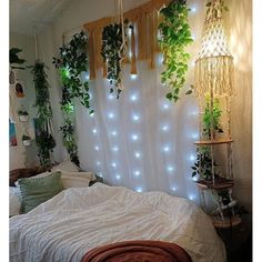 an unmade bed with plants on the wall and lights hanging from it's headboard