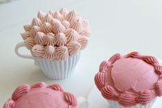 three cupcakes with pink frosting sitting on a table