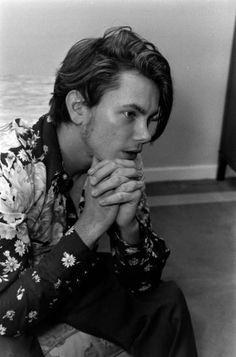 a black and white photo of a man sitting on the floor with his hands clasped