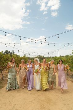 a group of women standing next to each other on top of a dirt road with string lights above them