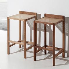 two wooden stools sitting next to each other in front of a white wall and floor