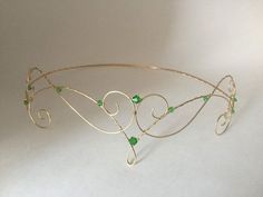 a gold tiara with green beads and wire work on the headband, sitting on a white surface