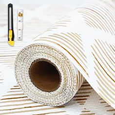 a roll of white and gold paper next to a ruler on a table with a pen