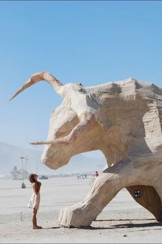 a woman standing next to a large wooden elephant statue on top of a sandy beach