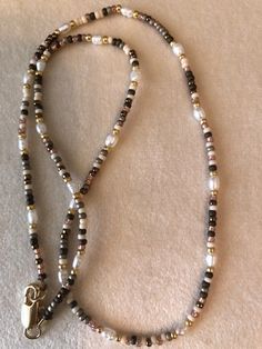 a long beaded necklace with a gold charm on it's end and a white ribbon around the clasp