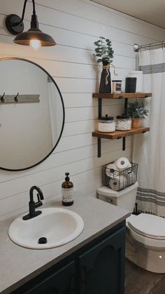 a white toilet sitting next to a bathroom sink under a round mirror on top of a wooden shelf