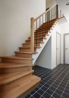 a wooden stair case next to a tiled floor in a room with white walls and black tiles