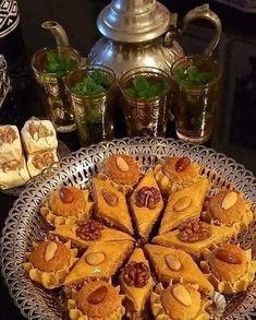 there are many pieces of dessert on the plate and some cups with tea in them