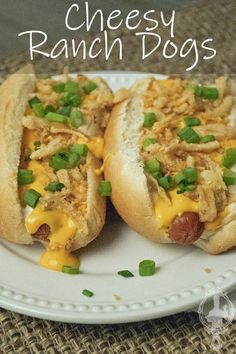 two cheesy ranch dogs on a white plate with green onions and cheese over them