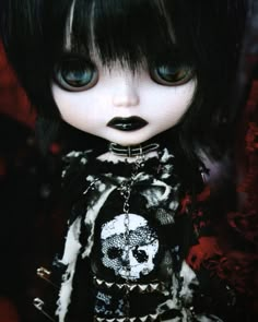 a close up of a doll with black hair wearing a dress and skull print on it