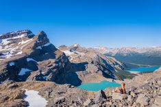 a woman sitting on top of a mountain next to a lake and snow covered mountains