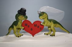 two dinosaur figurines holding a heart shaped sign