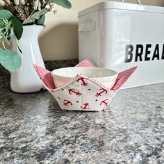 a paper boat sitting on top of a counter next to a vase with flowers in it