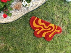 a red and yellow rug sitting on top of a grass covered field next to a potted plant