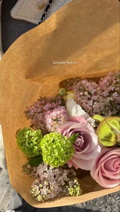 a bouquet of flowers sitting in a brown paper bag on the ground next to someone's feet