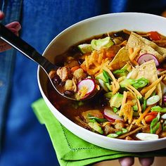 a person holding a bowl of chili and tortilla soup