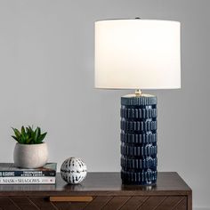 a table with a lamp, books and a plant on it in front of a gray wall