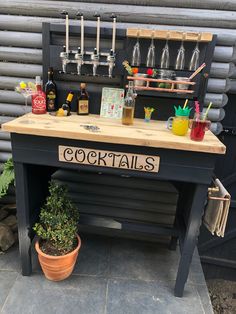 an outdoor bar with bottles and glasses on the top, next to a potted plant