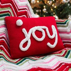 a red pillow with the word joy on it and a christmas tree in the background