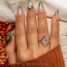 a woman's hand with green and white nail polish holding a ring on her finger