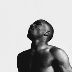 a man with no shirt on standing in front of a white wall and looking up