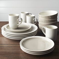 a table topped with white plates and cups next to each other on top of a wooden table