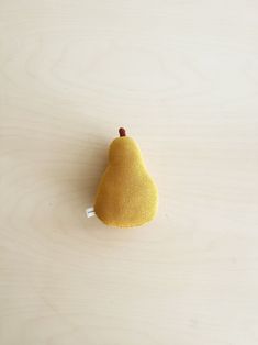 a small yellow pear sitting on top of a wooden table next to a white wall