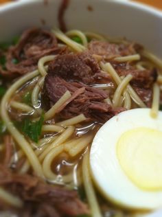 a bowl filled with noodles, meat and an egg