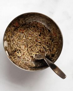 a metal bowl filled with food on top of a white counter next to a spoon