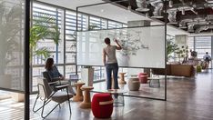 two people are standing in an office with glass walls and plants on the wall behind them