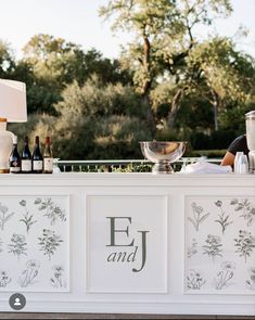 an outdoor bar with wine bottles and glasses on the counter, next to a lamp