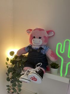 a pink teddy bear sitting on top of a shelf next to a potted plant