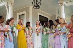 a group of women standing around each other in front of a house with bouquets