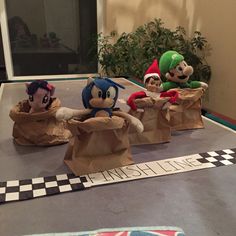 three paper bags that have stuffed animals in them on top of a table with a checkered floor