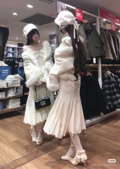 two women in white dresses and fur coats looking at clothes on display inside a store