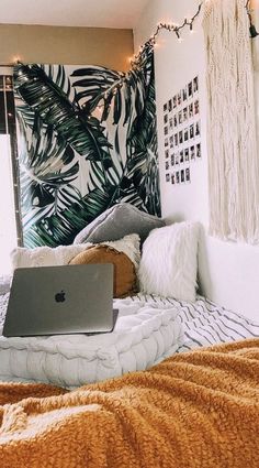 a laptop computer sitting on top of a bed next to a wall with palm leaves