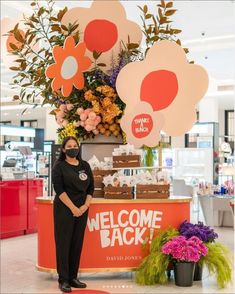 a woman standing in front of a welcome back sign with flowers and cake on it