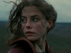 a close up of a person wearing a red coat and hair blowing in the wind