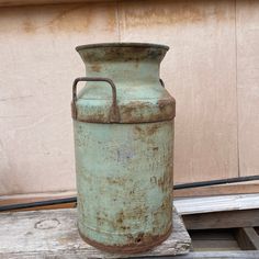 an old green metal container sitting on top of a wooden table next to a wall