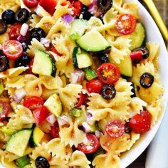 pasta salad with cucumbers, tomatoes and olives in a white bowl on a wooden table