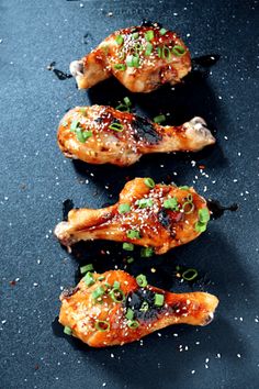 three pieces of chicken with sesame seeds and seasoning on the side, sitting on a black surface