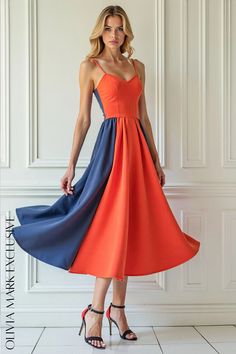 a woman in an orange and blue dress standing against a wall with her hands on her hips