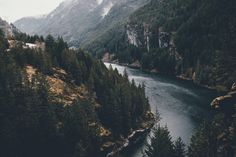 a river surrounded by mountains and trees in the middle of it's own area