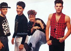 four young men standing next to each other in front of a white wall with one man wearing a plaid shirt