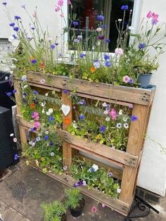 a wooden planter filled with lots of flowers on top of a cement floor next to a window