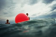 a man sitting on top of a red ball in the ocean