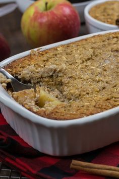 a close up of a casserole dish on a table with apples in the background