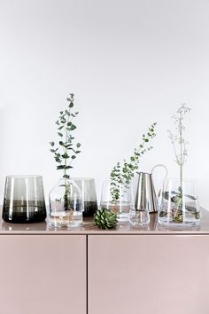 a table topped with vases and plants on top of a pink dresser next to a white wall