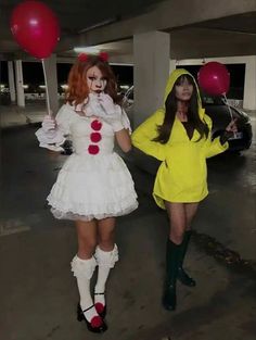 two women dressed in costumes walking through a parking lot with red and white balloons behind them